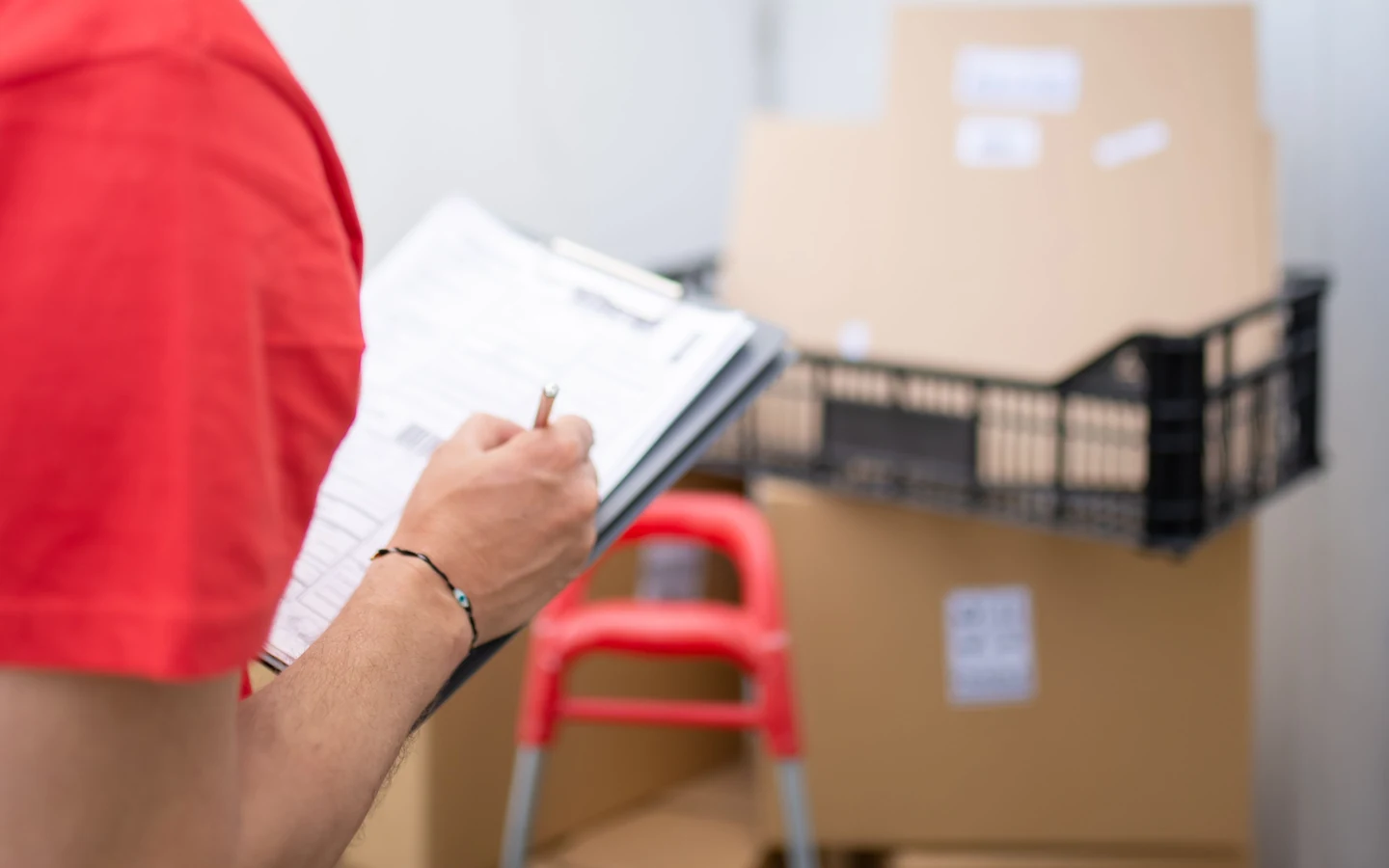 A worker checks a shipment checklist on a clipboard in front of packed cartons and a crate