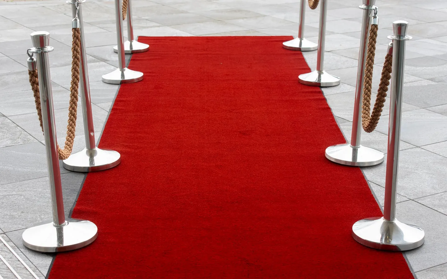 A red carpet between silver stanchions leading to an entrance
